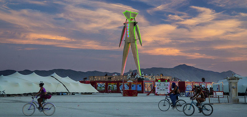 Tampilan patung kayu di tengah playa dalam acara Burning Man, terlihat juga tiga orang peserta tengah mengendarai sepeda